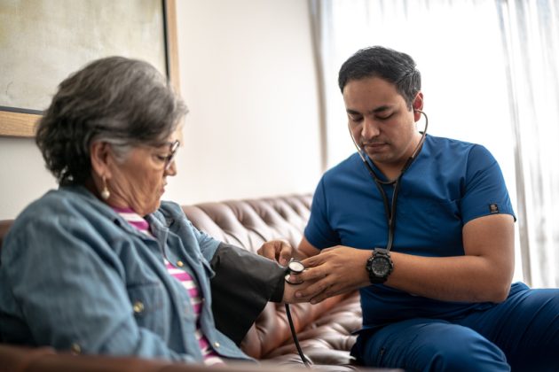 Mid adult nurse man measuring the senior woman pressure at nursing home