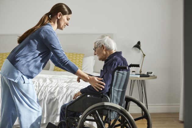 Nurse supporting senior man to sit on wheelchair.